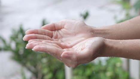 close up two hands wait to catch rain drops on rainy day, touch the nature, rains water on palms, slow motion, sustainable living concept, save and preserve water energy and natural recourses,