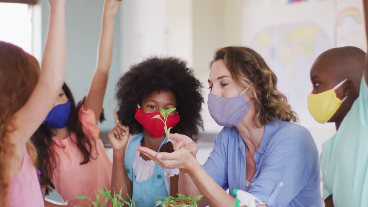 Professora de máscara facial mostrando uma muda de planta aos alunos na sala de aula