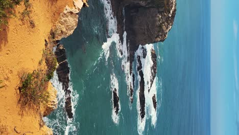 Zambujeira-do-Mar-over-the-sea-shore-with-ocean-waves,-cliffs-and-sand-dunes-covered-by-green-vegetation-red-leaves-of-sour-fig,-sunny-day,-clear-blue-sky