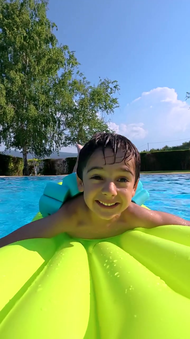 Happy Young Boy Smiling and Playing on an Inflatable Float in a Swimming Pool
