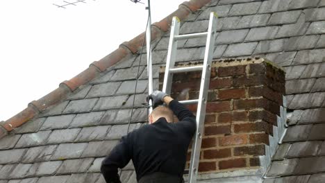 hombre en la escalera de montaje de la antena de televisión en el techo de la chimenea de casa