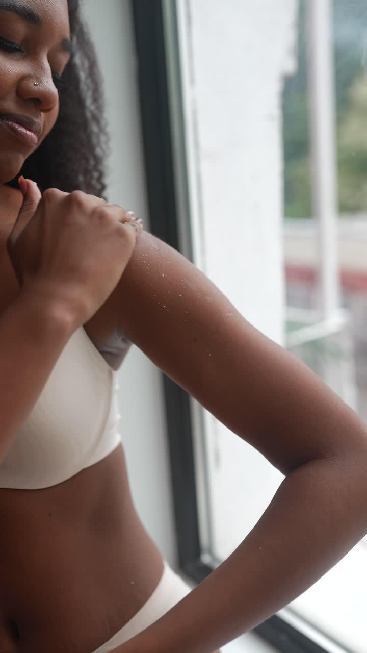 mujer aplicando crema en su brazo junto a una ventana
