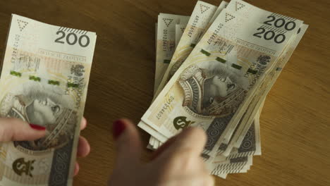 female hands counting 200 polish zloty bills at table - banking and finance, budget concept, close-up shot