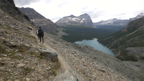 a young couple briskly backpacking along a steep narrow trail above lake o'hara, alberta, canada.