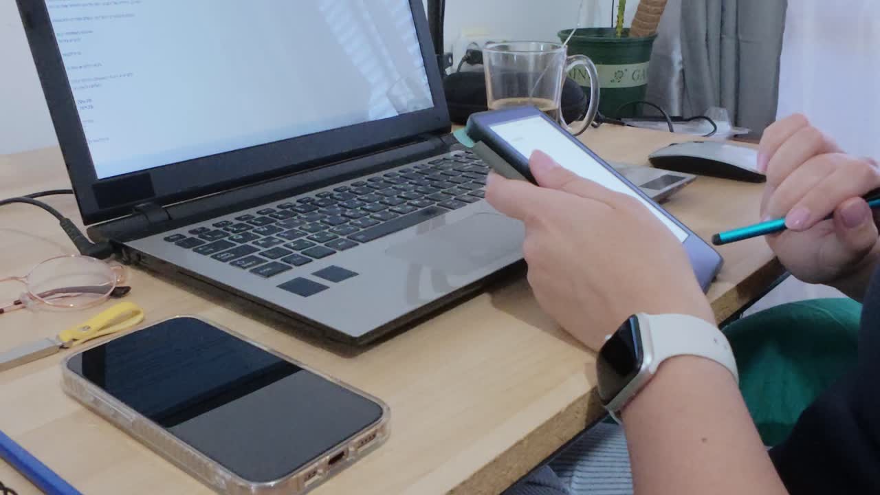 A modern desk setup with hands using a tablet, laptop, smartphone, coffee, and smartwatch.