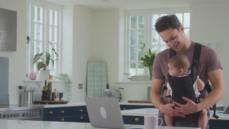 Padre-Transgénero-Trabajando-Desde-Casa-En-Una-Computadora-Portátil-Cuidando-A-Su-Hijo-En-Cabestrillo