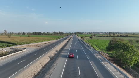 drone following a car riding on a multi lane road of panamericana norte peruvian highway through farming fields on both corners and birds flying in the sky