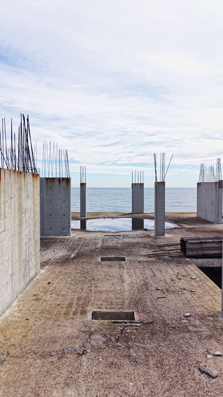 Concrete remnants stand tall against a cloudy sky by the serene ocean, creating a hauntingly beautiful scene of unfinished dreams and urban exploration