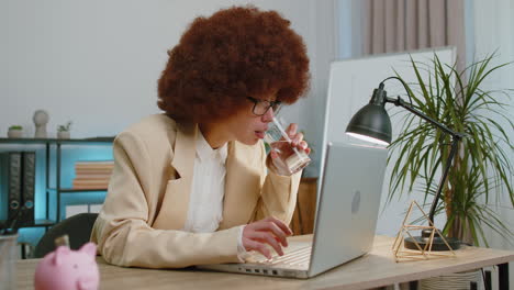 Focused-business-woman-girl-at-office-reads-social-media-news-accidentally-spilled-water-on-laptop