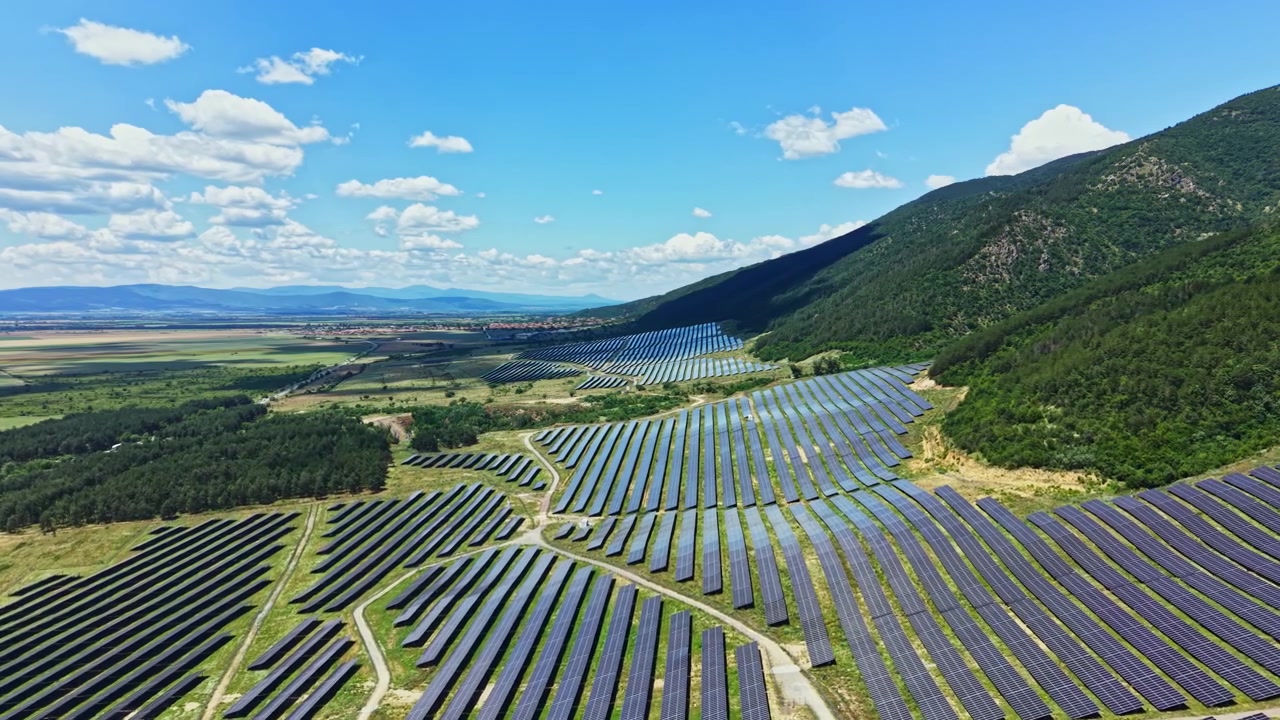 Solpaneler dækker et stort område på en mark nær bakker og viser produktion af vedvarende energi på en klar solskinsdag.