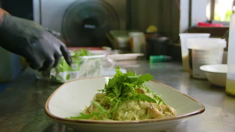 chef puts finishing touches of arugula green leaves on seafood pasta with shrimp, thumbs up sign as they finish