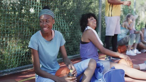 feliz equipo de baloncesto femenino diverso entrenando con un entrenador masculino en una cancha soleada, en cámara lenta