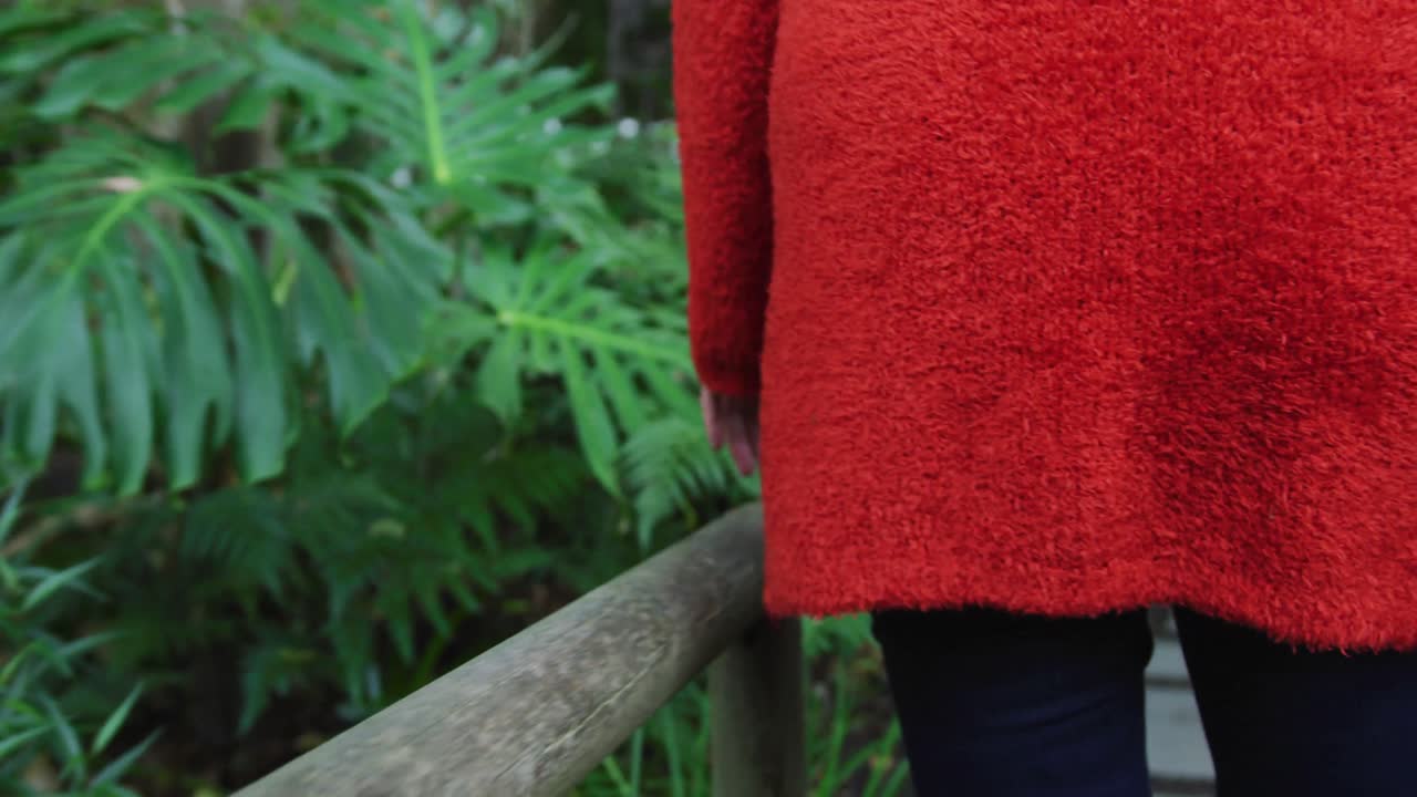 뒷면 보기 고위 백인 여성의 중간 부분이 휴식을 취하고, 정원에서  ⁇ 고 식물에 손을 대고 있습니다.