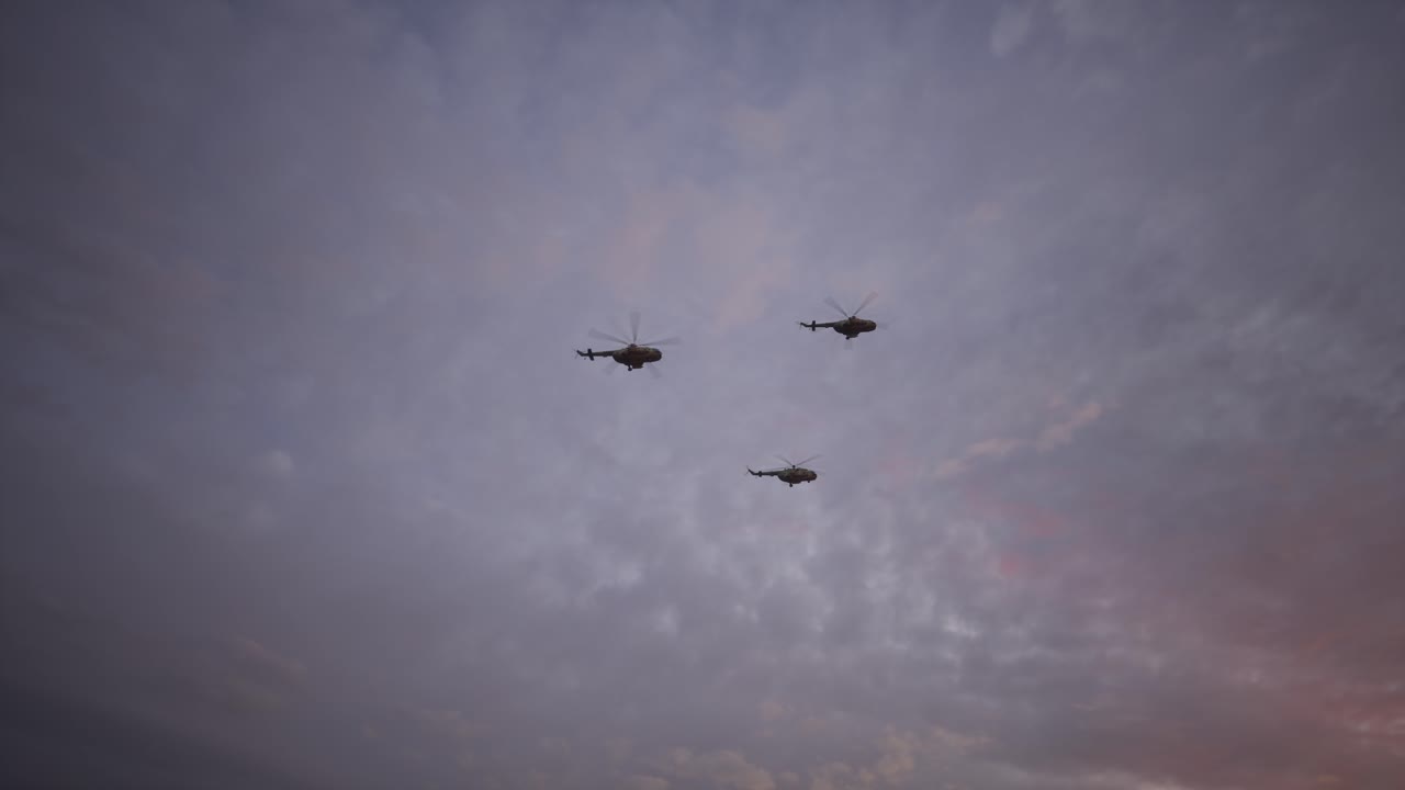 Militærhelikopter i formasjonsflygning ved solnedgang eller soloppgang gjennom skyet himmel.