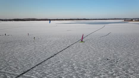 aerial tracking shot of sailing ship yacht skates on frozen iced lake during sun in winter
