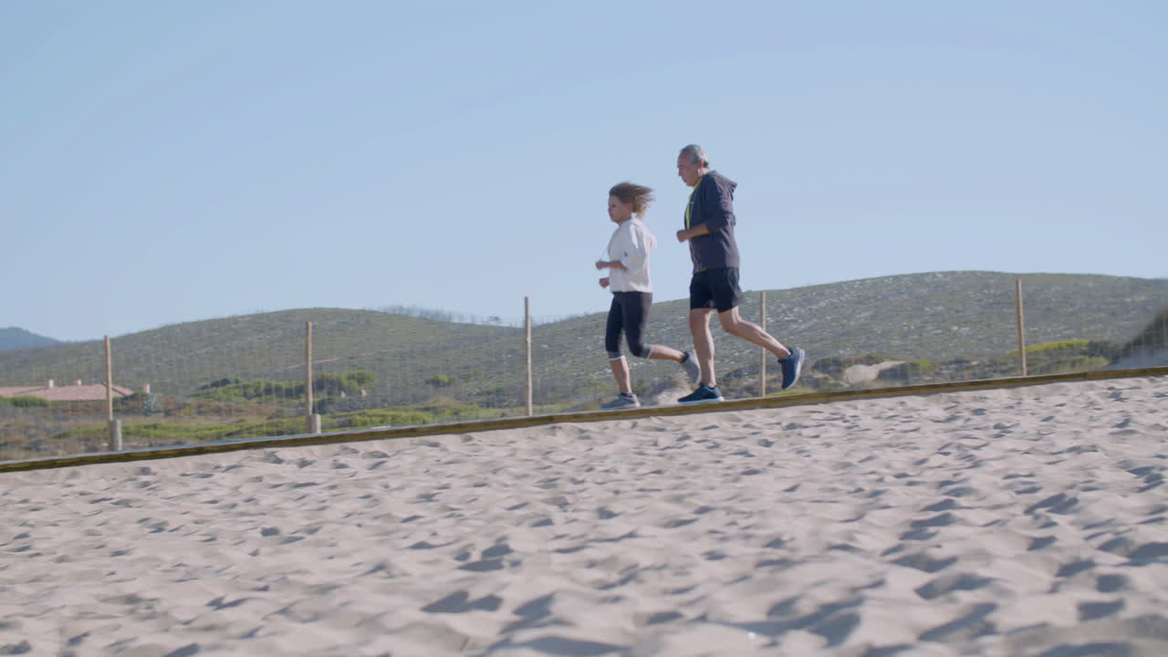 Allegra coppia di anziani che corre lungo un sentiero su una spiaggia sabbiosa.