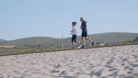 Una-Alegre-Pareja-De-Ancianos-Corriendo-Por-El-Camino-En-La-Playa-De-Arena