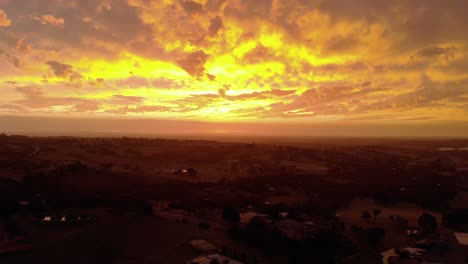 forward moving aerial shot of the bright orange glow of the sun setting on the horizon in rural australia