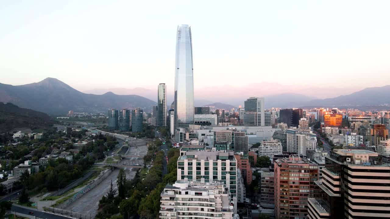 Riprese aeree che si innalzano sopra gli edifici del quartiere di Providencia, con i grattacieli della moderna area di Sanhattan e le colline all'ora blu, Santiago, Cile.