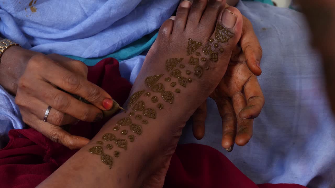 Un'inquadratura di mani femminili che dipingono un piede nero con l'henné