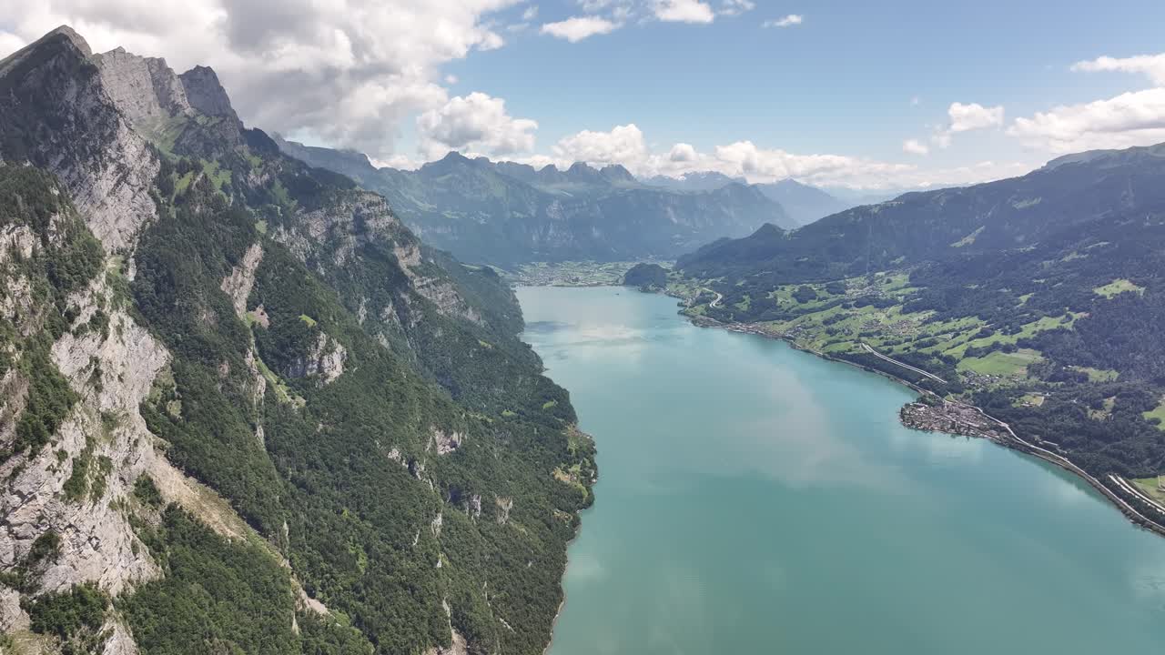 Aerial view over Weesen and Walensee in Switzerland, where turquoise waters meet steep alpine cliffs and rolling green valleys under a bright sky