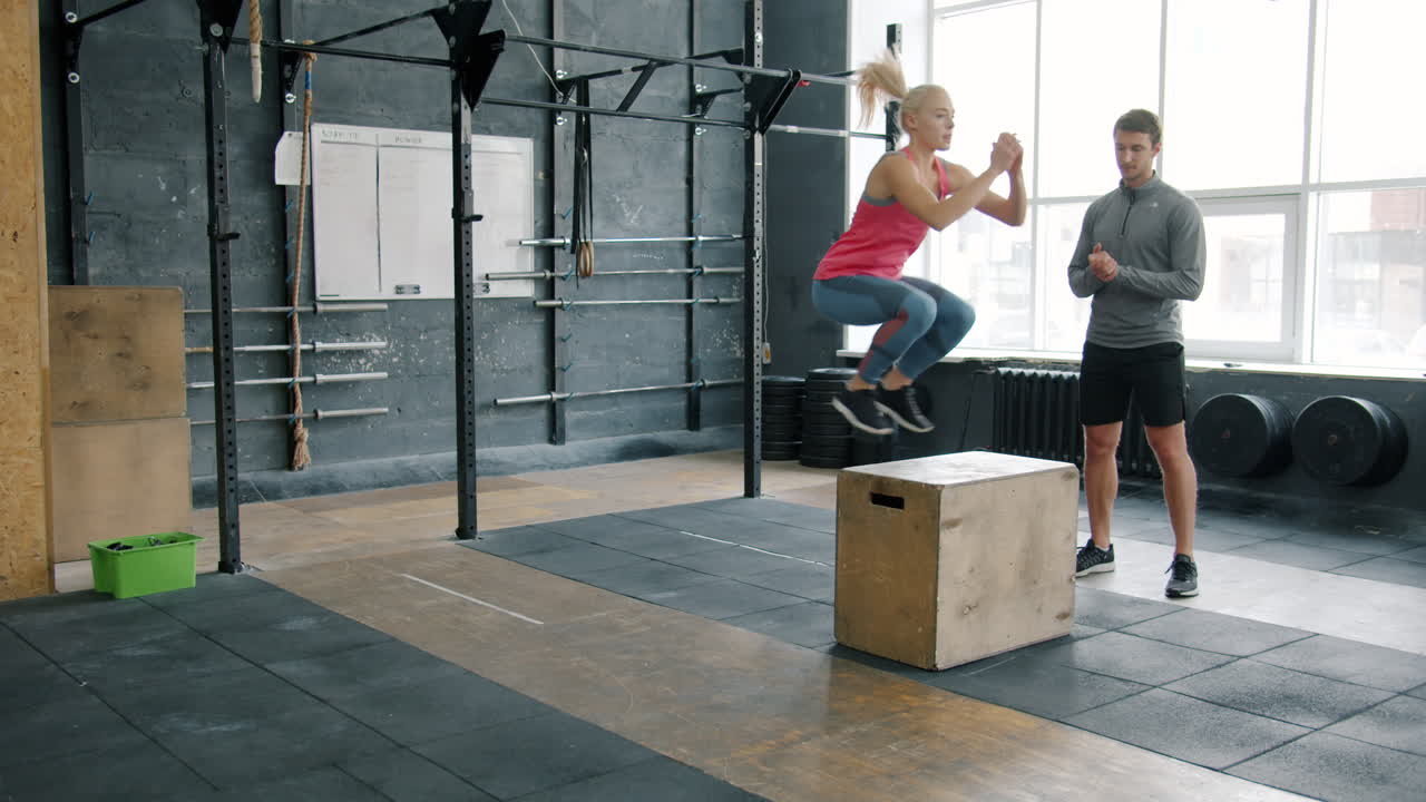 Woman Performing Box Jumps with Personal Trainer in Gym