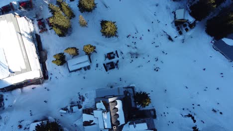 static top down aerial clip of a busy mountain ski resort with skiers and snowboarders passing by amenities, snowploughs and a cable car station near sofia, bulgaria