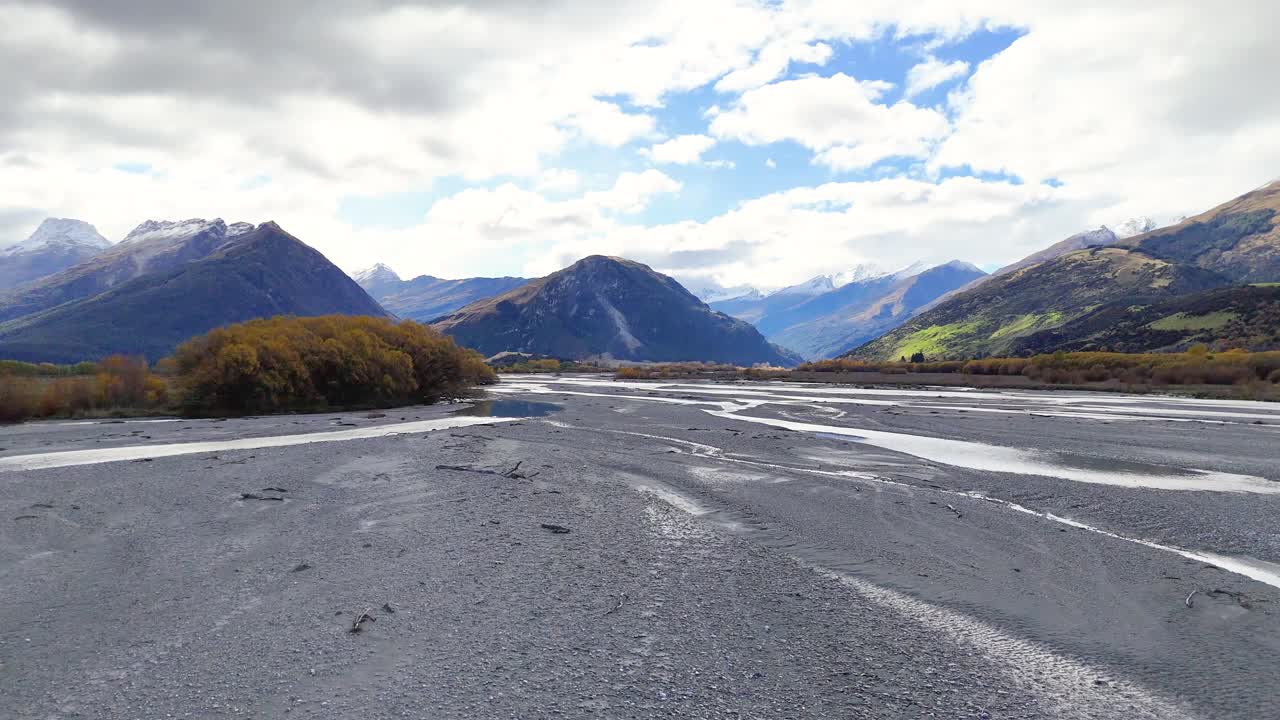 A tranquil riverbed with mountains and trees under a partly cloudy sky, showcasing natural beauty and calmness