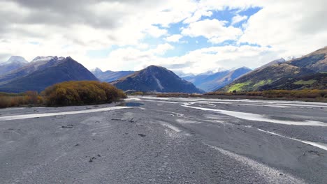 a tranquil riverbed with mountains and trees under a partly cloudy sky, showcasing natural beauty and calmness