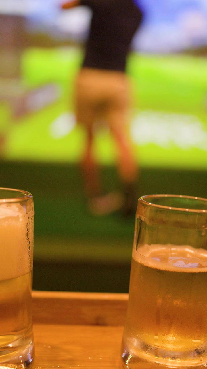 Primo piano di boccali di birra su un tavolo di legno mentre un uomo gioca a golf virtuale al coperto.