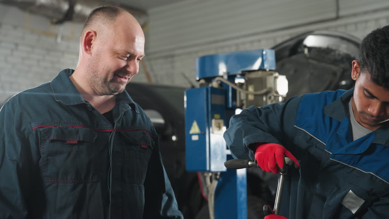 ingeniero en taller mecánico trabajando en el motor de automóvil, apretando la tuerca con guantes rojos mientras el colega observa y guía, características de fondo del automóvil, herramientas mecánicas y equipos de taller