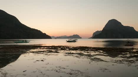 Vuelo-Aéreo-Hacia-Atrás-Que-Muestra-Un-Bote-Estabilizador-Con-Puesta-De-Sol-Y-Hora-Dorada-En-El-Nido,-Palawan,-Filipinas