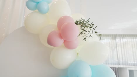 close up of pastel balloon cluster with green leaves in bright indoor party setting