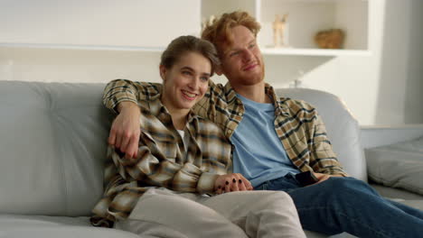 happy marriage enjoying tv program. smiling ginger man embracing cute girlfriend