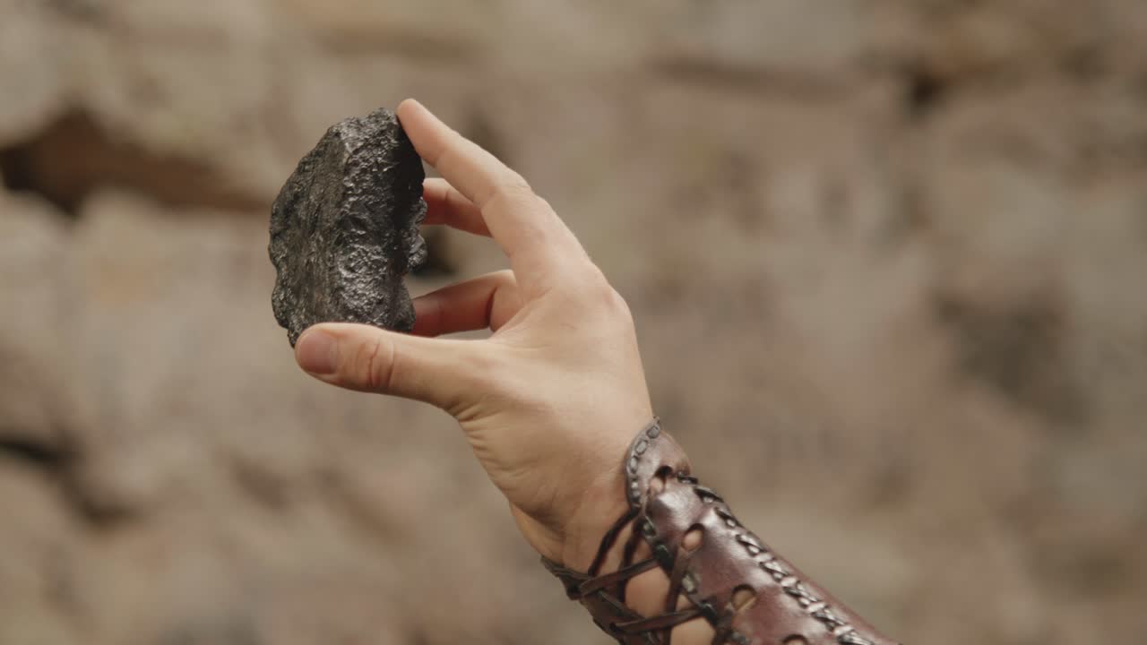 A close-up shot of a hand inspecting a raw, black mineral. Historical, fantasy, or geology concept, showing the discovery of a valuable resource like coal or obsidian