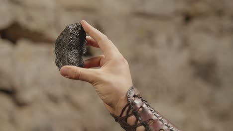 a close-up shot of a hand inspecting a raw, black mineral. historical, fantasy, or geology concept, showing the discovery of a valuable resource like coal or obsidian
