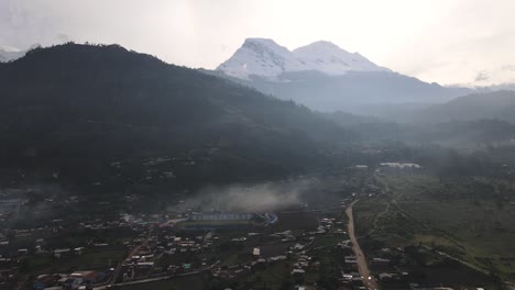 A-backlit-drone-shot-of-Huascaran-peak-and-a-huge-green-hill-located-in-the-peruvian-andes