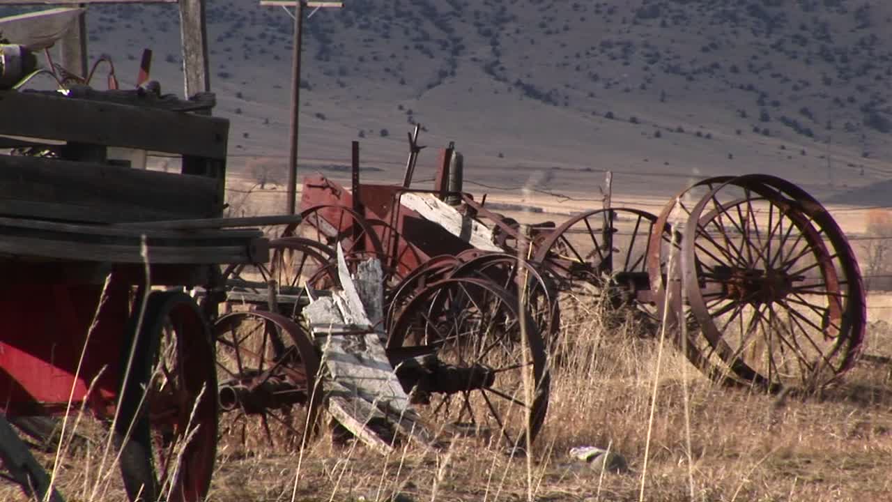 las llantas de rueda de carro vintage rotas y oxidadas y otros equipos antiguos se abandonan en la hierba seca de la pradera