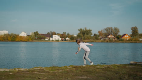 active girl throws pebble into water turning around on shore