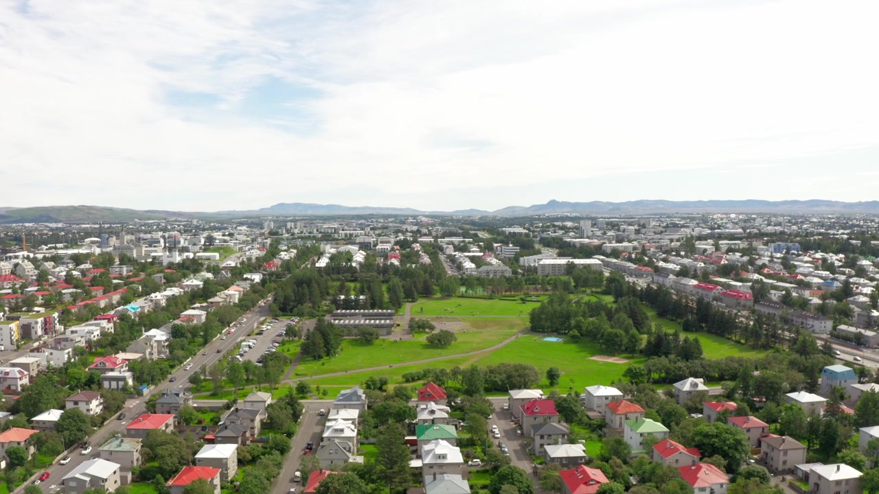 Veduta aerea di Reykjavik, Islanda, che mostra case residenziali colorate, un grande parco verde e il paesaggio urbano con montagne distanti sotto un cielo nuvoloso