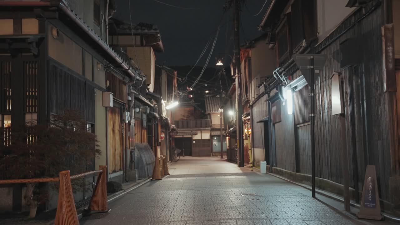 A dimly lit alley in Kyoto at night, lined with traditional buildings and glowing lanterns, creates a moody and atmospheric scene in the historic city.