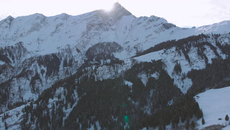 Aerial-drone-shot-as-turning-to-the-right,-showing-high-snowy-mountains-day-time-as-the-sun-shines-in-the-lense