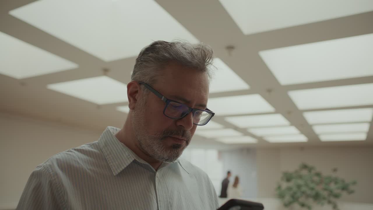 Uomo d'affari di mezza età concentrato che usa il telefono cellulare in un ufficio moderno