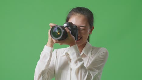 스튜디오에서 녹색 스크린 배경에 서서 사진을 찍고 미소 짓는 카메라를 사용하는 아시아 사진작가의 클로즈업