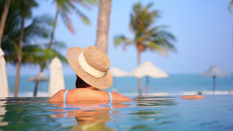 back of a woman in the swimming pool of a tropical hotel in miami, blurred umbrellas and sea on background, florida beach