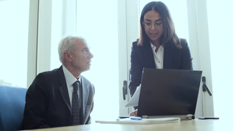 serious female assistant explaining paper details to male boss