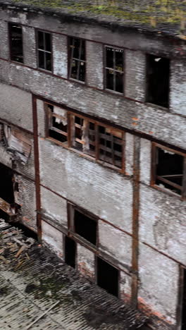 ruined architecture after military actions. abandoned building with broken windows and many hole in walls. damaged building outdoors. aerial view. vertical video