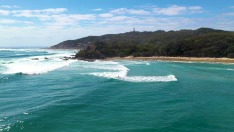 Breite-Drohnenaufnahme-Von-Surfern-Im-Wasser-Und-Insel-Im-Hintergrund-Am-Strand-Von-Wategos,-Australien