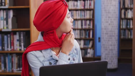 Eine-Asiatische-Studentin,-Die-Einen-Roten-Hijab-Trägt-Und-In-Einer-Bibliothek-Studiert-Und-Einen-Laptop-Benutzt