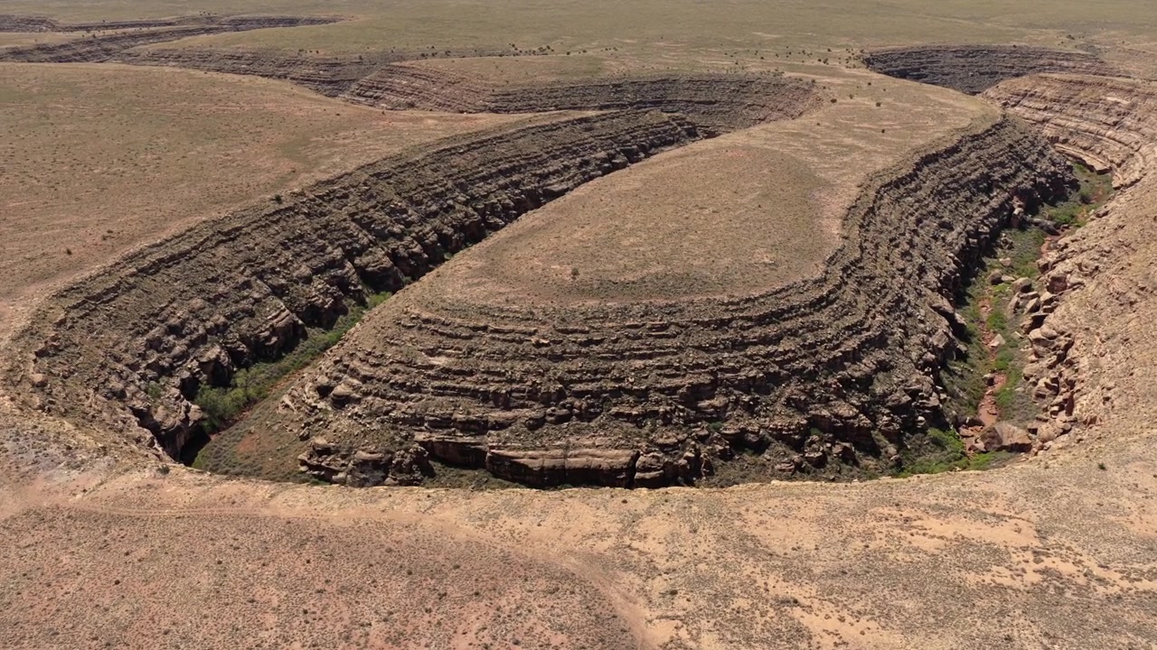Voo de drone 4K UHD exibindo um cânion de rio seco enorme e sinuoso no deserto do Arizona. Um pequeno carro preto em uma trilha de terra remota destaca a escala épica deste destino de viagem de aventura robusto.